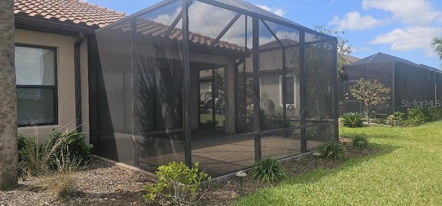 back of house with a lawn, glass enclosure, stucco siding, and a tiled roof
