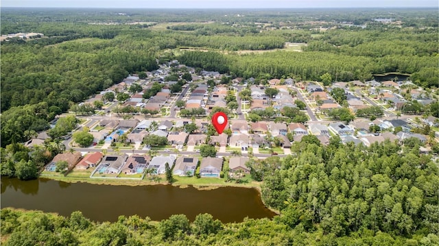 aerial view of property and surrounding area featuring a large body of water, a forest, and nearby suburban area