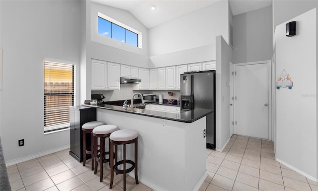 kitchen featuring black fridge, dark countertops, high vaulted ceiling, light tile patterned flooring, and a breakfast bar area