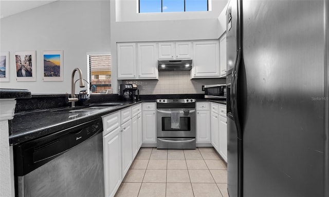 kitchen featuring stainless steel appliances, under cabinet range hood, high vaulted ceiling, light tile patterned floors, and dark countertops