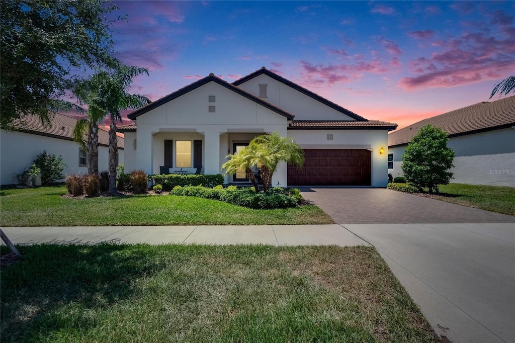 view of front of property with driveway, a tiled roof, an attached garage, a front yard, and stucco siding