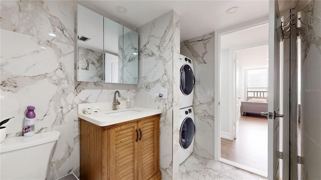 400 Island Way Unit 210, Clearwater Beach, FL 33767 - bathroom featuring stacked washer / dryer, marble tiled floors, stone wall, toilet, and vanity