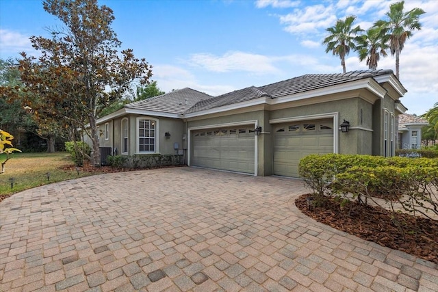 view of front of property with an attached garage, stucco siding, decorative driveway, and central AC