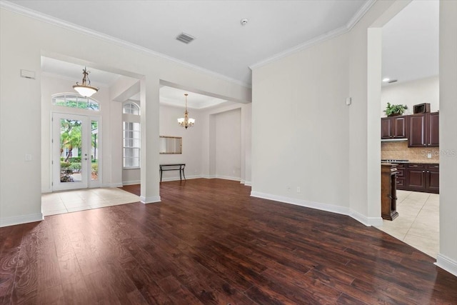 unfurnished living room featuring light wood finished floors, an inviting chandelier, visible vents, and crown molding