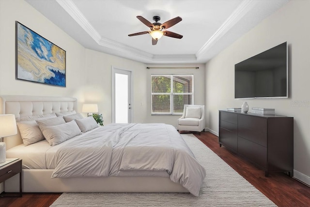bedroom featuring dark wood-type flooring, crown molding, ceiling fan, a tray ceiling, and baseboards