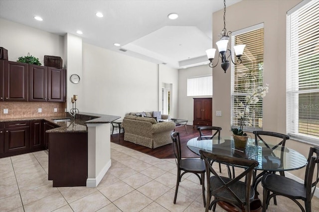 kitchen featuring a sink, a peninsula, tasteful backsplash, a chandelier, and light tile patterned floors