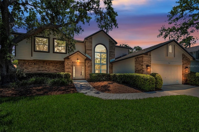 traditional-style house featuring an attached garage, a lawn, driveway, and brick siding