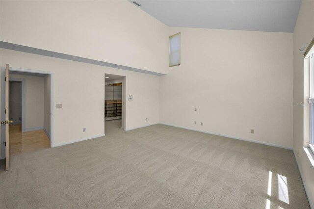 spare room with high vaulted ceiling, light carpet, and baseboards
