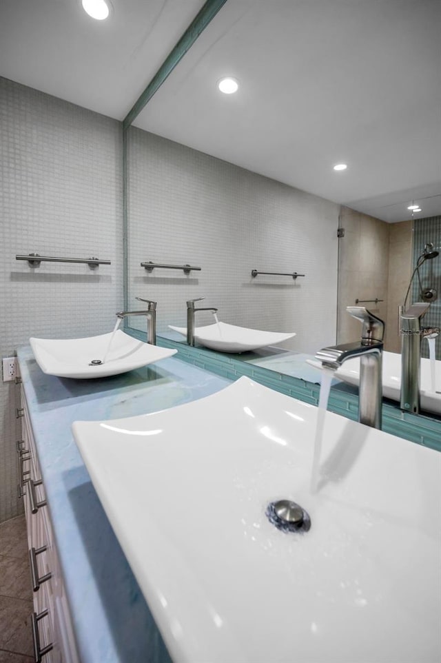 bathroom with recessed lighting, double vanity, tile walls, and a sink