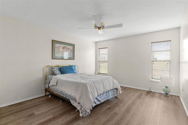 bedroom featuring baseboards, a textured ceiling, wood finished floors, and multiple windows