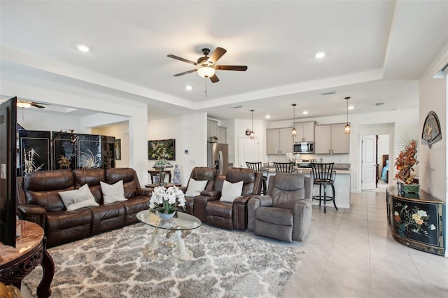 living area with a ceiling fan, a tray ceiling, and light tile patterned floors