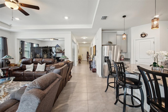 living room with visible vents, a ceiling fan, a tray ceiling, and light tile patterned floors