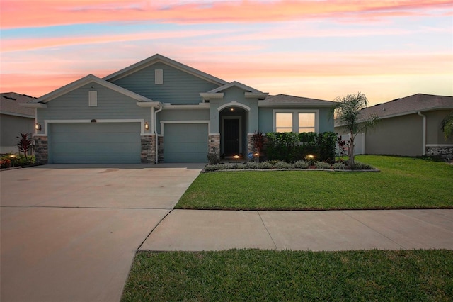 view of front facade featuring driveway, stone siding, a garage, a yard, and stucco siding
