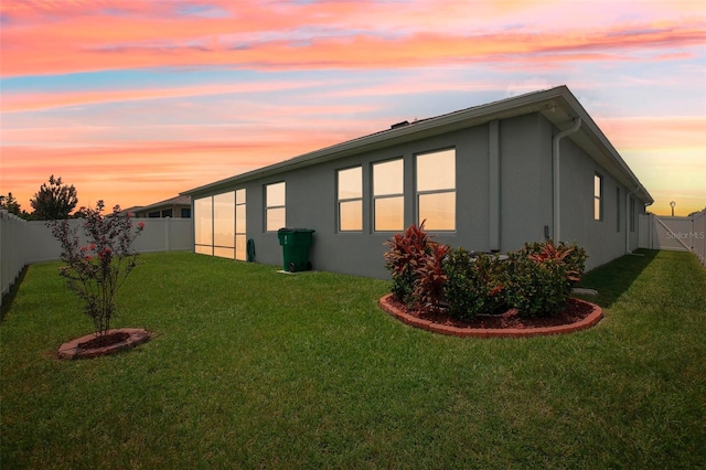 property exterior at dusk featuring a fenced backyard, a yard, and stucco siding