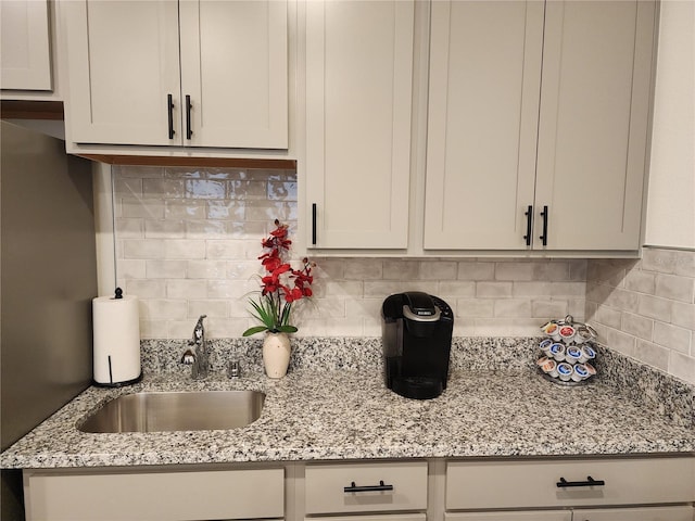 kitchen featuring backsplash, light stone countertops, and a sink