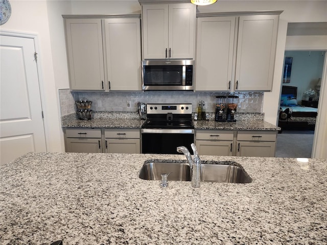 kitchen with stainless steel appliances, a sink, light stone counters, and gray cabinets