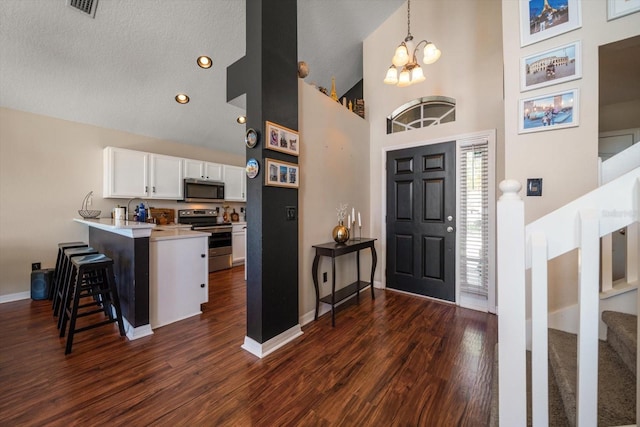 entryway with high vaulted ceiling, a notable chandelier, stairway, and dark wood-style flooring