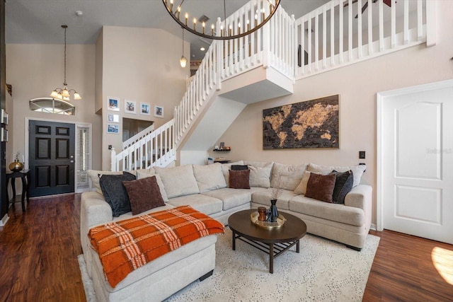 living area featuring stairway, wood finished floors, a towering ceiling, baseboards, and a notable chandelier