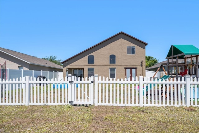 rear view of property with fence, stucco siding, a gate, and a playground