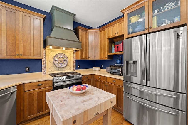 5902 Audubon Manor Blvd, Lithia, FL 33547 - kitchen featuring stainless steel appliances, custom exhaust hood, light wood-style floors, glass insert cabinets, and a textured ceiling
