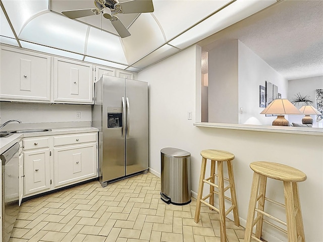 kitchen featuring appliances with stainless steel finishes, light countertops, a ceiling fan, white cabinetry, and a kitchen bar