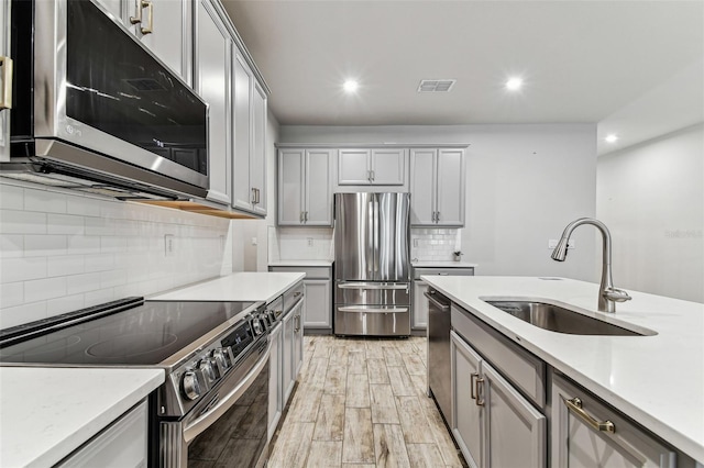 kitchen featuring gray cabinetry, a sink, appliances with stainless steel finishes, and light countertops