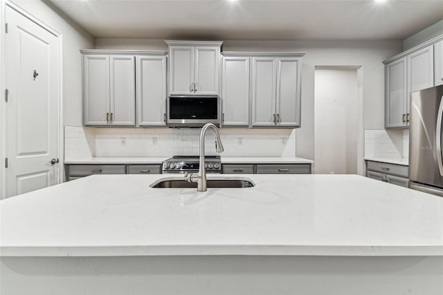 kitchen featuring gray cabinetry, a sink, backsplash, and appliances with stainless steel finishes