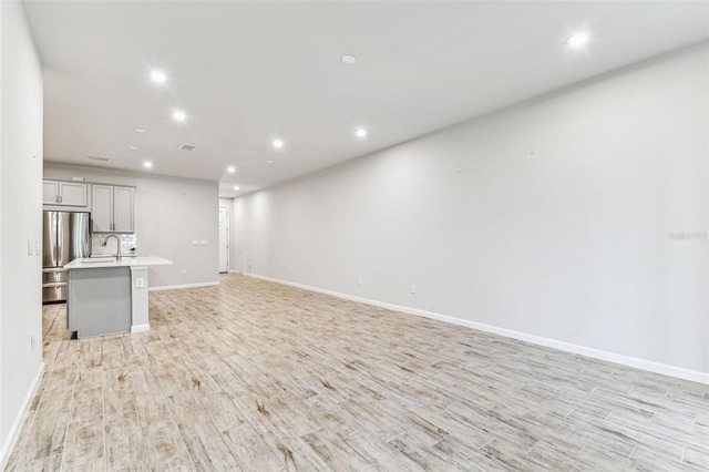 unfurnished living room featuring a sink, recessed lighting, light wood-style flooring, and baseboards