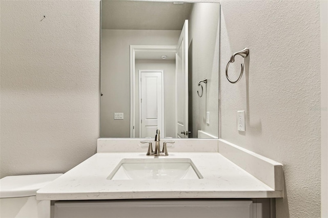bathroom with toilet, a textured wall, and vanity