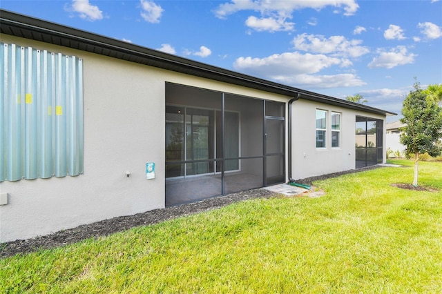 rear view of property with stucco siding, a yard, and a sunroom