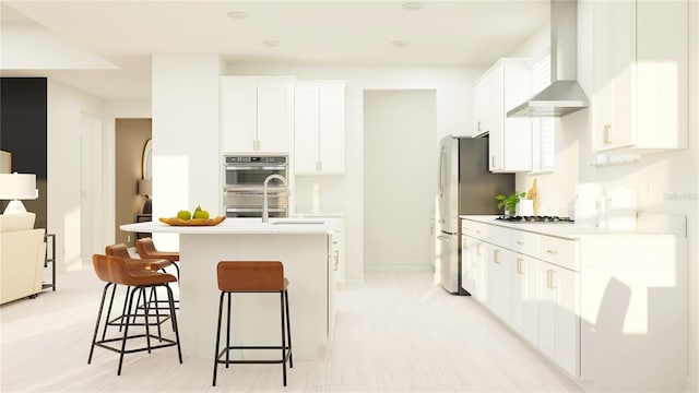 kitchen featuring wall chimney exhaust hood, light countertops, a sink, a breakfast bar, and appliances with stainless steel finishes