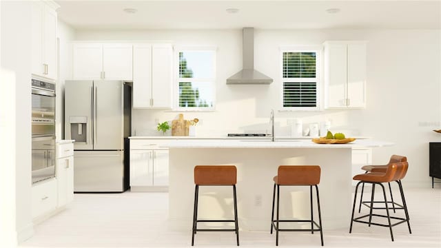 kitchen with a sink, a center island with sink, white cabinetry, fridge with ice dispenser, and wall chimney range hood