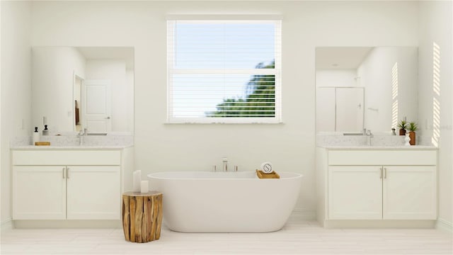 full bathroom with a freestanding bath, two vanities, baseboards, and a sink