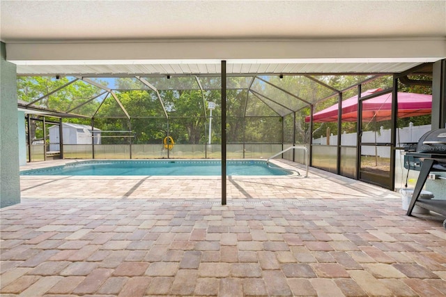 outdoor pool with a lanai, a storage unit, an outbuilding, and a patio