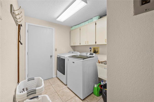 laundry area with washer and clothes dryer, a textured wall, light tile patterned floors, cabinet space, and a textured ceiling