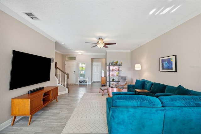 living room featuring crown molding, light wood finished floors, stairs, and visible vents