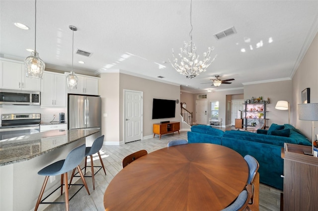 dining room featuring visible vents, ornamental molding, stairs, light wood-style flooring, and ceiling fan with notable chandelier