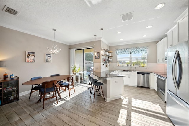 kitchen with visible vents, crown molding, appliances with stainless steel finishes, and a kitchen breakfast bar