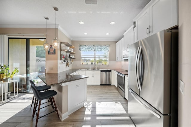 kitchen featuring crown molding, a peninsula, white cabinetry, a sink, and stainless steel appliances