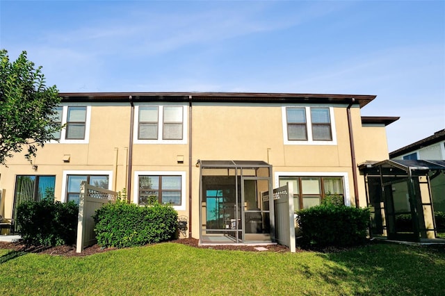 rear view of property featuring a lawn, a sunroom, and stucco siding