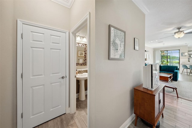 corridor featuring crown molding, light wood finished floors, and baseboards