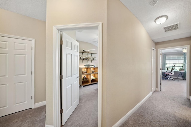 hallway featuring carpet floors, baseboards, a textured ceiling, and visible vents
