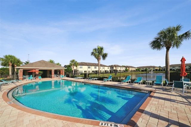 community pool with a patio area, fence, and a residential view