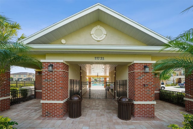 view of exterior entry with brick siding, a gate, fence, and stucco siding