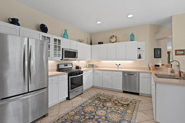 kitchen with light tile patterned floors, stainless steel appliances, light countertops, white cabinets, and a sink