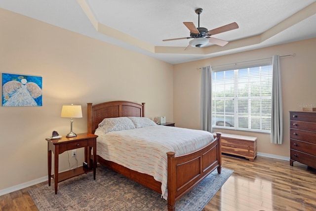 bedroom featuring baseboards, a raised ceiling, ceiling fan, and wood finished floors