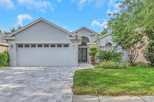 single story home with decorative driveway, a garage, stucco siding, and a front yard