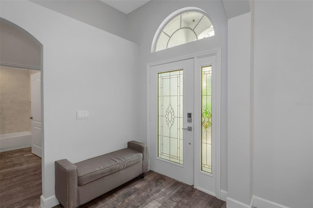 foyer entrance featuring arched walkways, baseboards, and dark wood finished floors