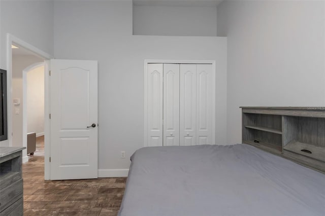bedroom featuring arched walkways, baseboards, dark wood finished floors, and a closet