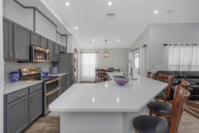 kitchen featuring gray cabinets, visible vents, appliances with stainless steel finishes, a large island with sink, and a sink